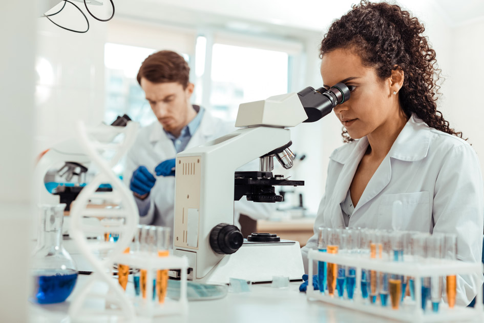 A black woman and caucasian man work together with microscopes in a science lab